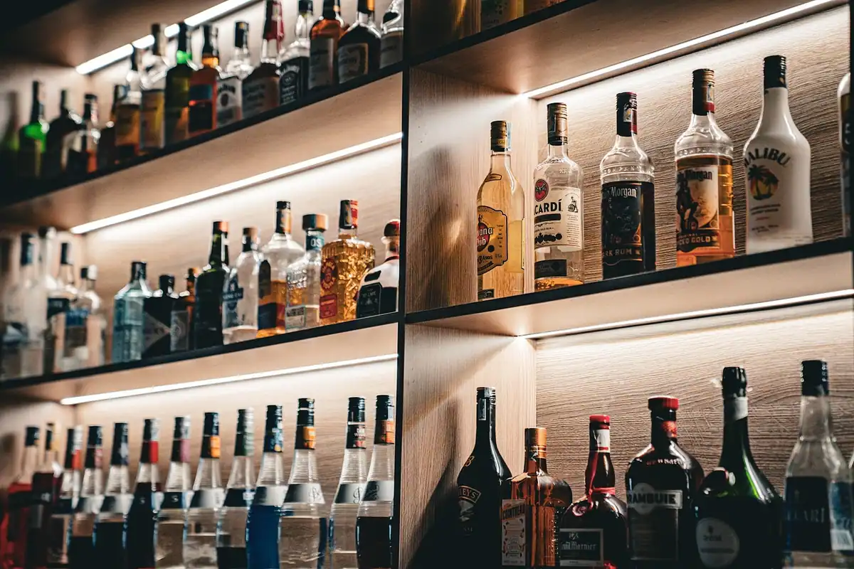 Sticle de băuturi alcoolice aliniate pe rafturile unui bar, într-o lumină caldă