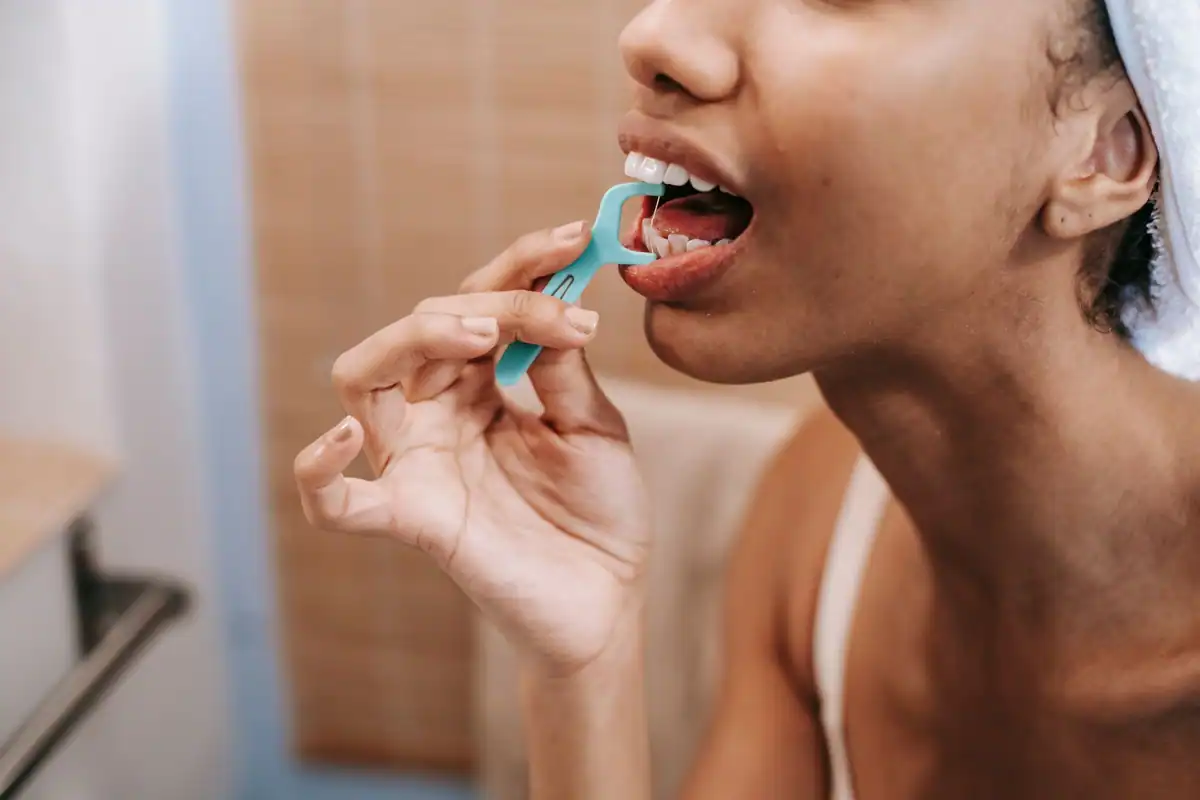 Femeie care folosește un dispozitiv cu ață dentară pentru a curăța spațiile dintre dinți