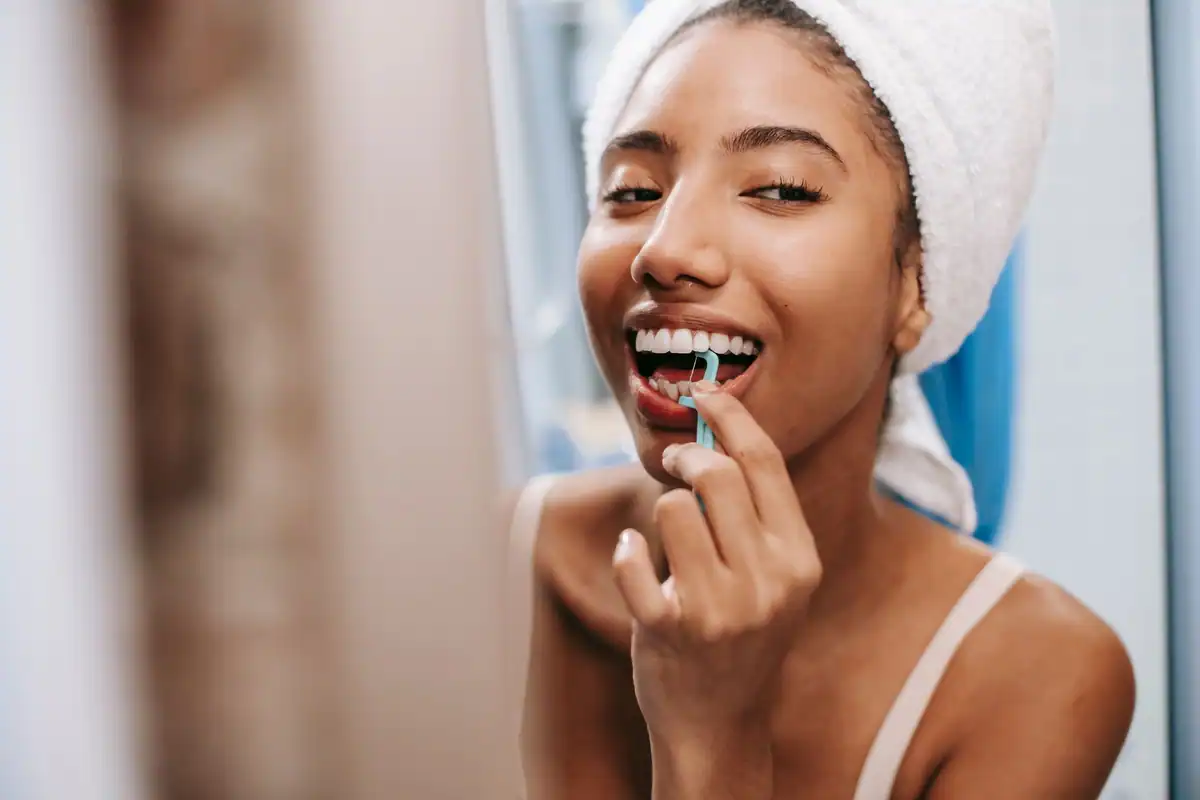 Femeie zâmbitoare, cu prosop pe cap, care folosește ața dentară în baie