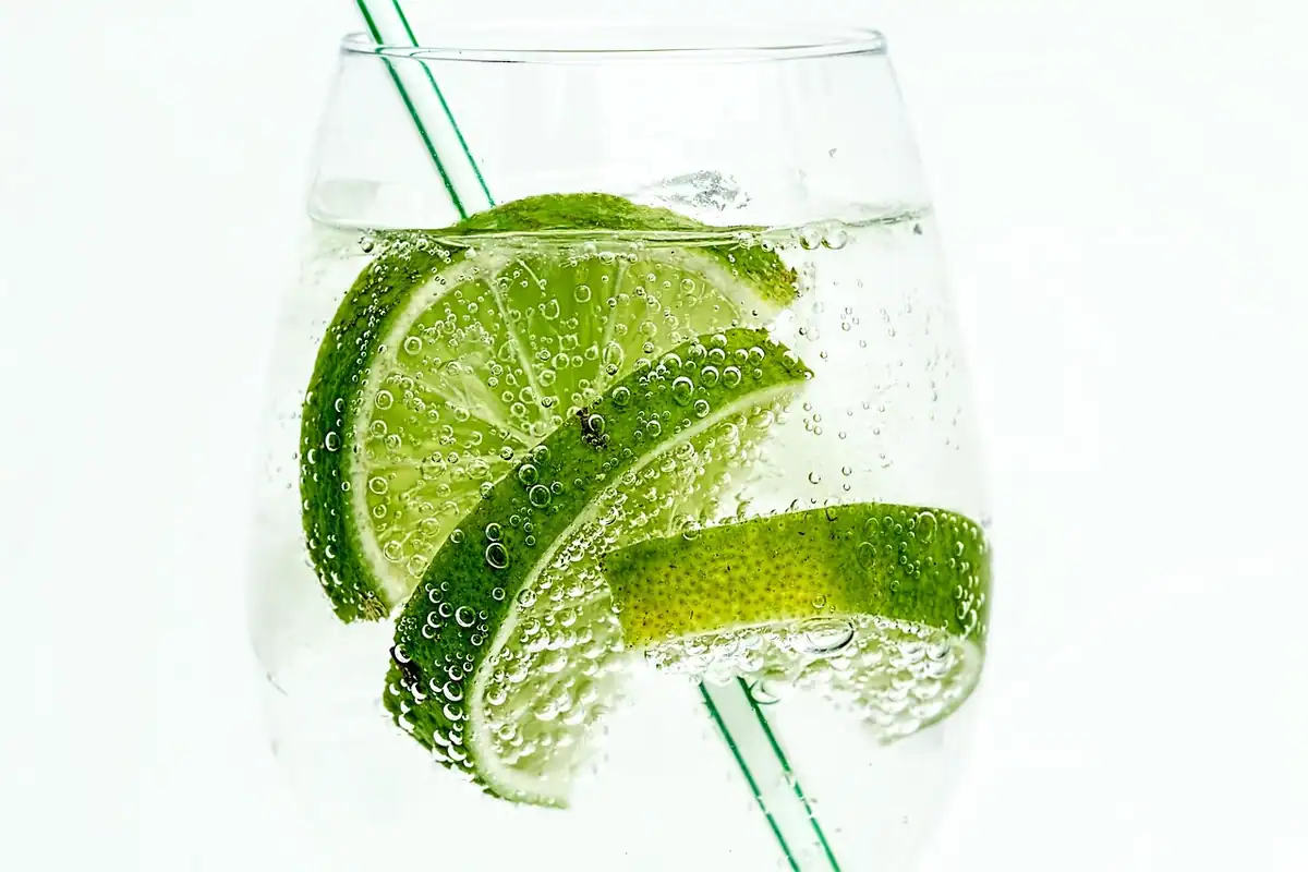 Pahar cu limonadă cu felii de lime, cuburi de gheață și un pai, o băutură rece