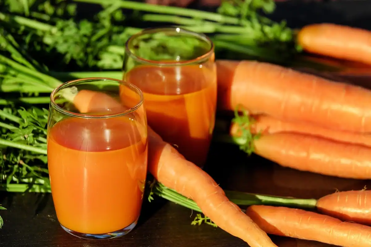 Pahare cu suc proaspăt de morcov, alături de morcovi întregi, o băutură cu vitamine