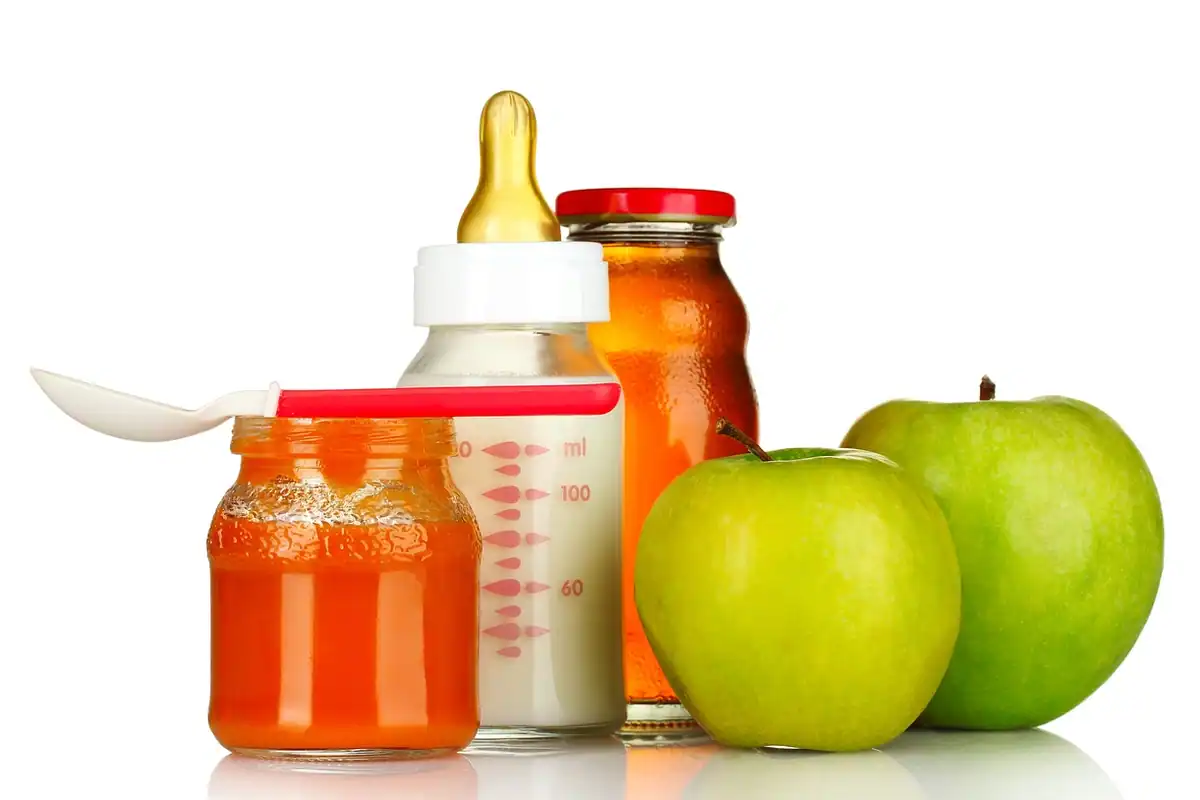 Biberon lângă borcane cu piure de fructe și mere verzi pe fundal alb