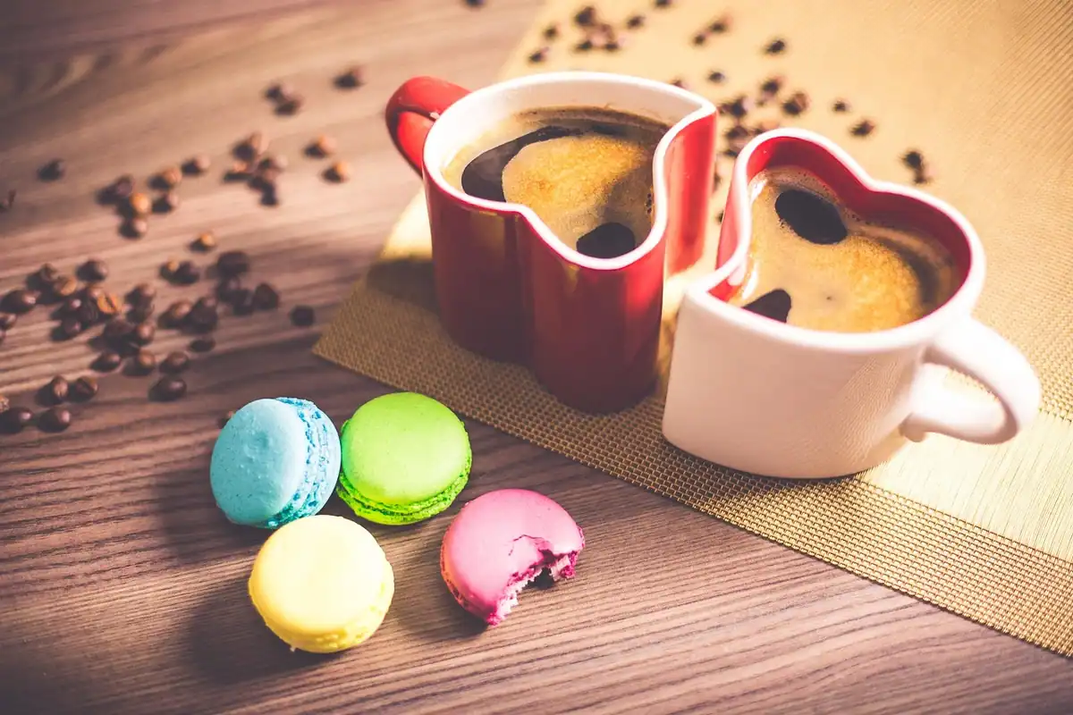 Cești colorate cu cafea neagră și macarons pe o masă, într-un prim-plan