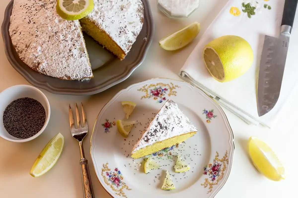Felie de tort cu lămâie și zahăr pudră pe o farfurie, lângă un cuțit