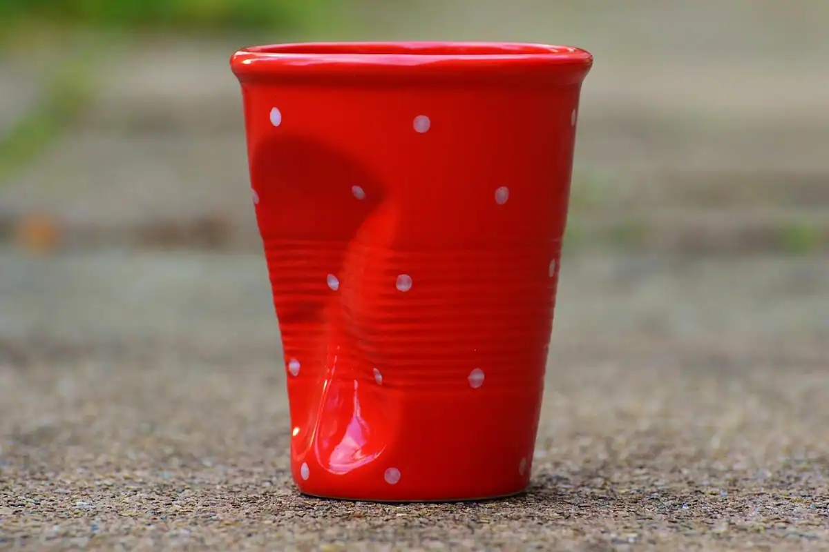 Cană de ceramică roșie cu aspect șifonat, pentru cafea, fotografiată de aproape