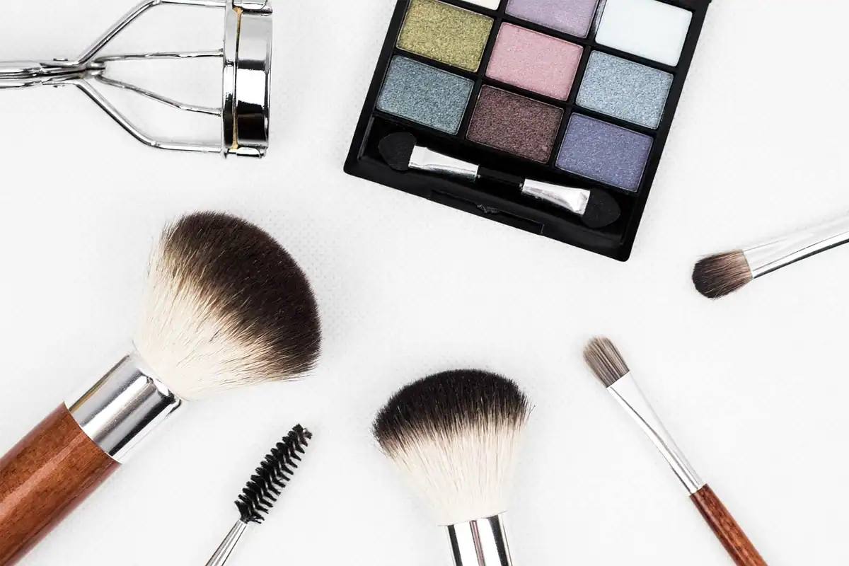 Pensule de machiaj și produse cosmetice aranjate pe un fundal neutru, văzute de sus
