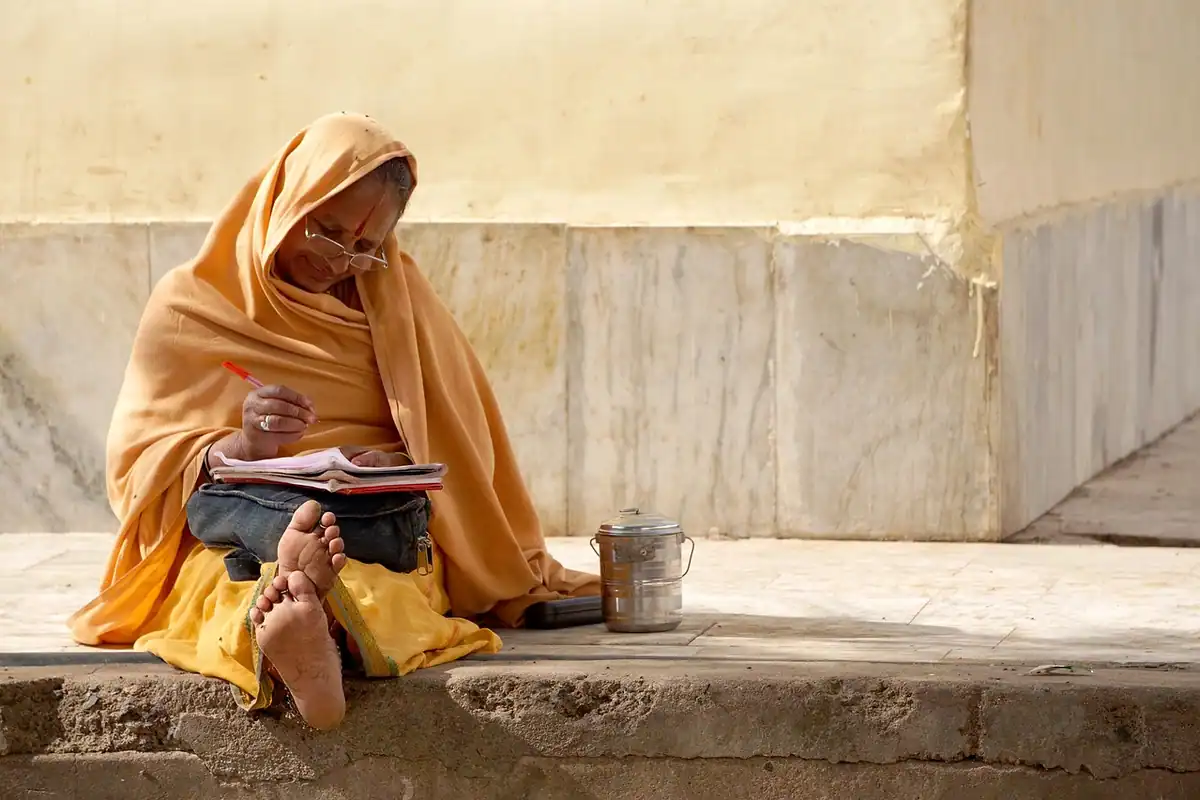 Femeie în haine tradiționale indiene care scrie, așezată pe o stradă din Delhi