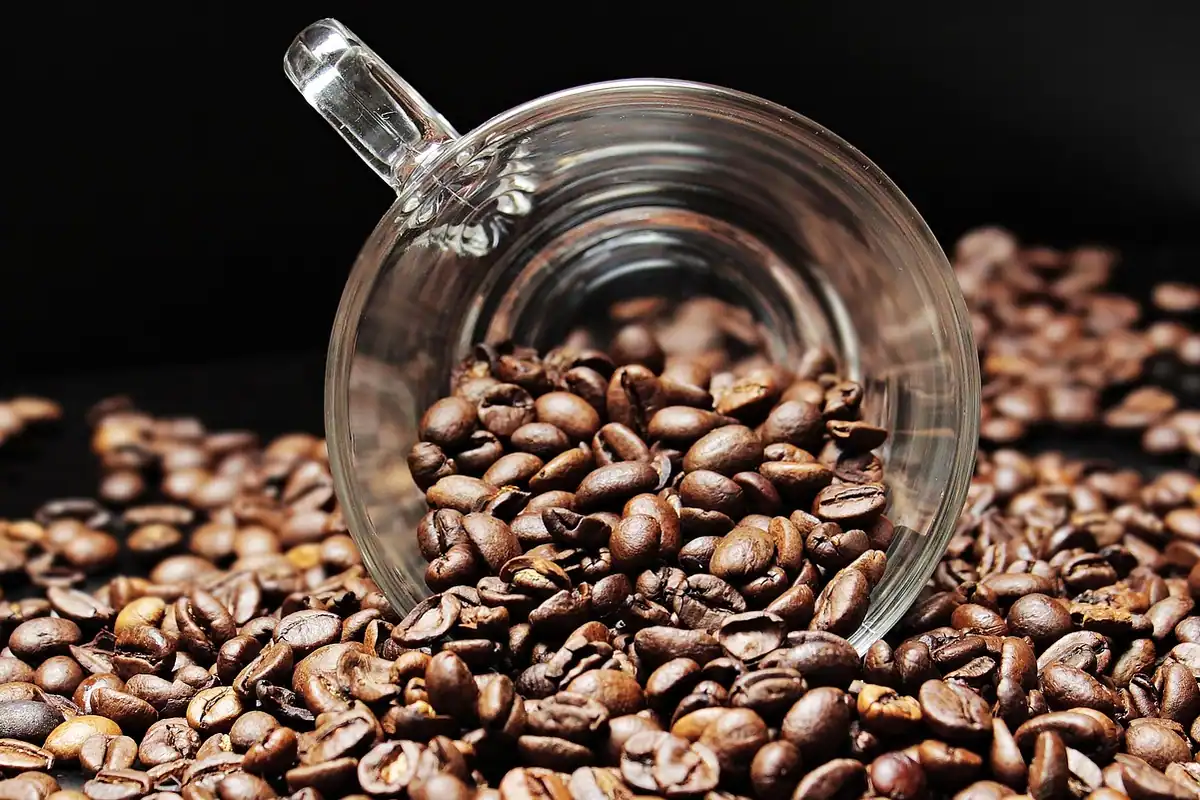 Pahar răsturnat din care se revarsă boabe de cafea prăjită pe fundal închis
