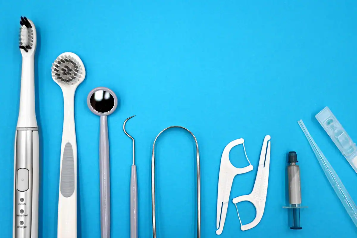 Periuțe, oglindă dentară, ață și racletă pentru limbă pe fundal albastru