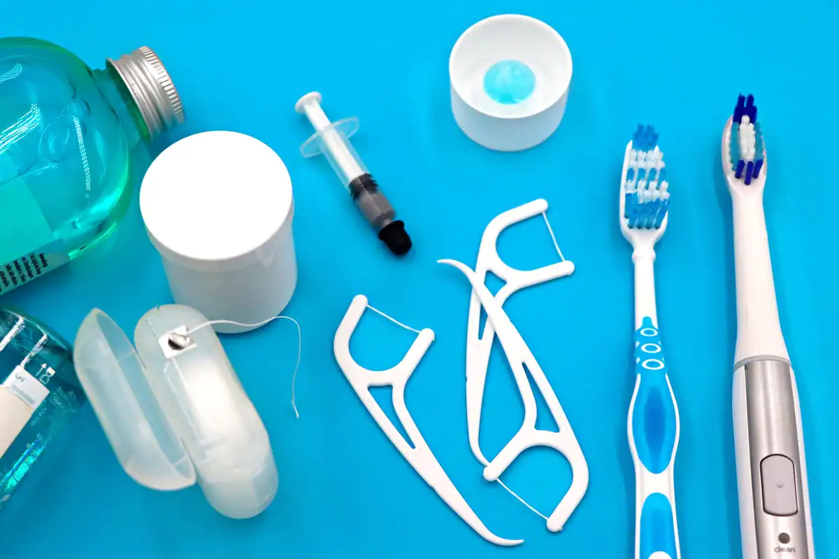 Ață dentară, bețișoare interdentare și periuțe așezate ordonat pe o suprafață albastră