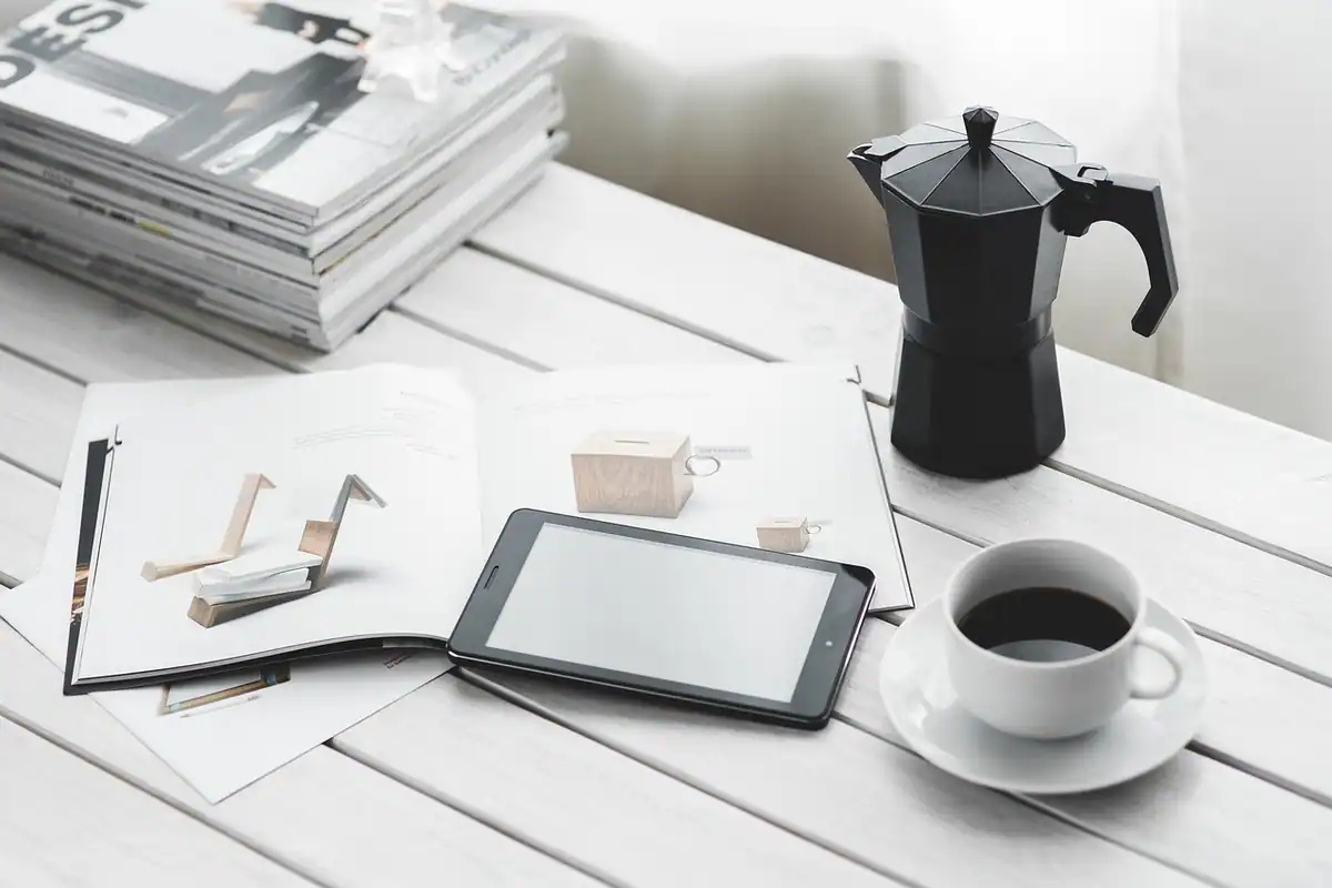 Tabletă digitală lângă o ceașcă de cafea și reviste, pe un birou