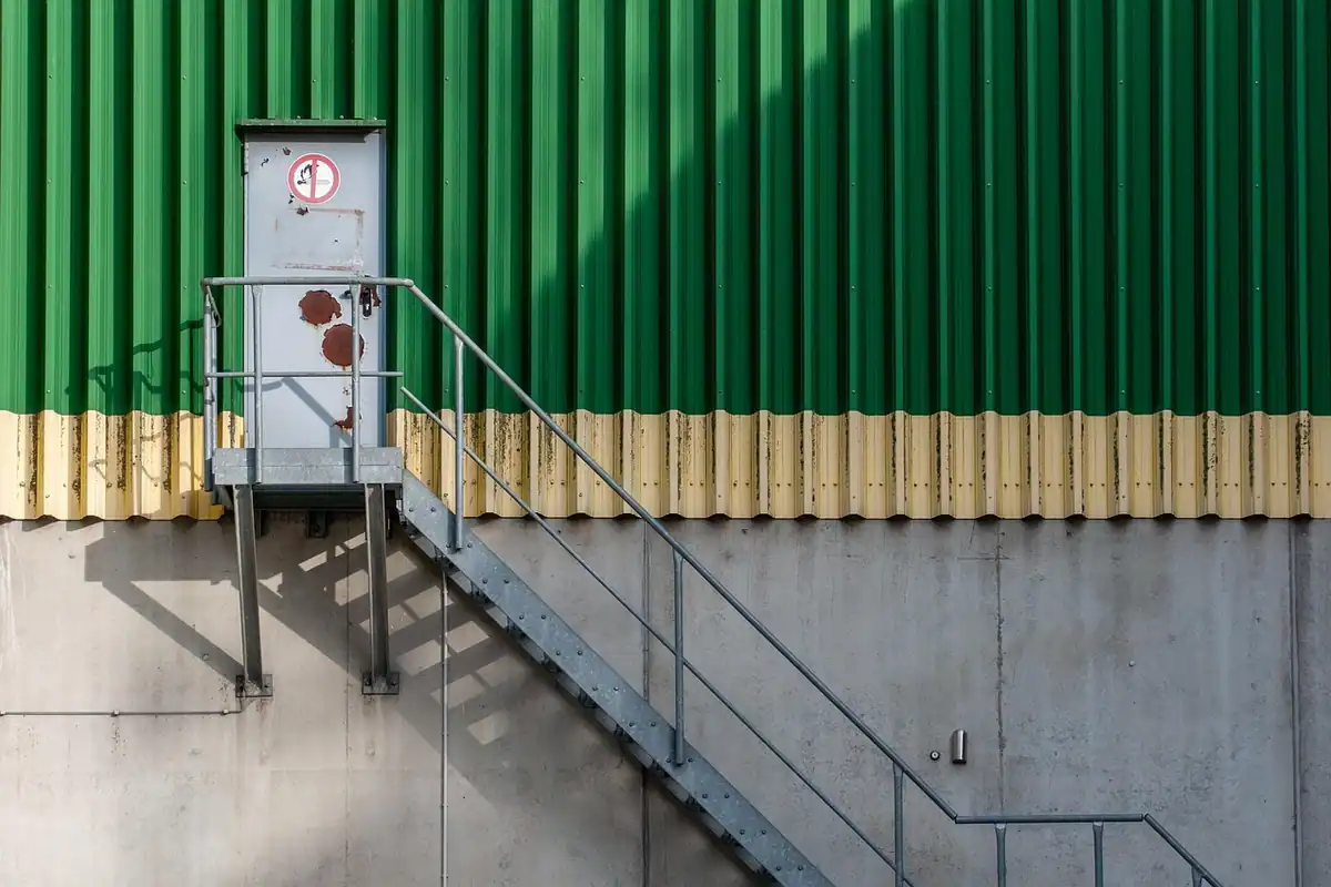 Fațadă de clădire industrială cu scări și ușă verde, de tip depozit